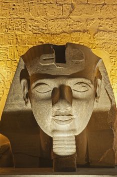 Large statue head of Ramses II at entrance to ancient egyptian Luxor Temple lit up during night