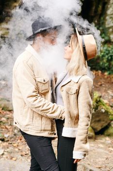 Couple in vape cloud. Two in smoke. Tourists in cold autumn forest with vape. Man and women in smoke. Two smokers. Beautiful couple in fog. E-cigarettes and people