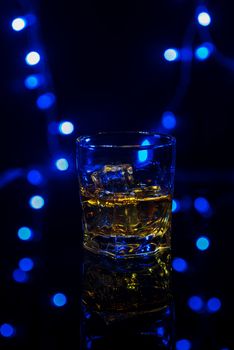 Glass of whiskey on the rocks with some ice on the table. Concept of hard liquor. With festive holiday bokeh