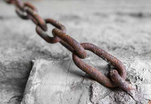 Rusty chain anchored to the cement pole. Defocused blurry background.