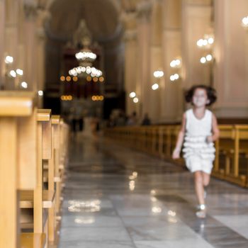 A little girl runs to church, heading for the altar. Defocused blurry background.