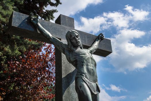 A statue of Jesus Christ crucified against dramatic sky. Jesus Christ on cross. Jesus christ statue in the cemetery.