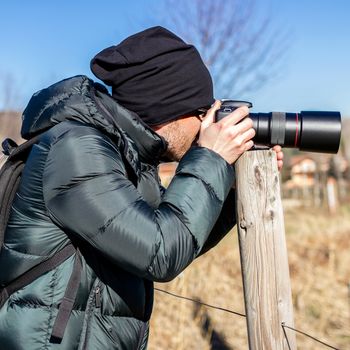 Closeup of photographer with digital camera outdoors. Young man photographer photographing nature. Shallow DOF.