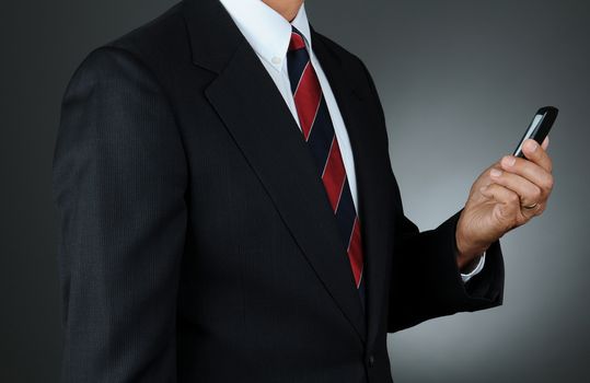 Closeup of a businessman checking messages on his cell phone. Horizontal format over a light to dark gray background. Man is unrecognizable.
