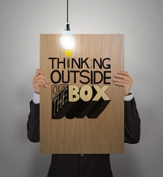 man showing poster of hand drawn word THINKING OUTSIDE OF THE BOX with growing lightbulbon wooden board as concept 