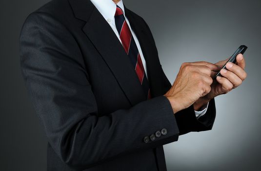 Closeup of a businessman dialing his cell phone. Horizontal format over a light to dark gray background. Man is unrecognizable.