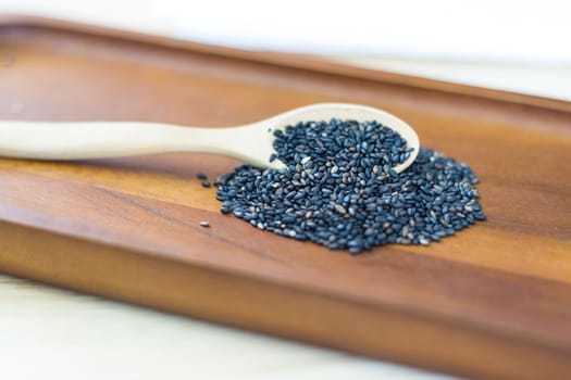 Black sesame seeds in wooden spoon pile on wood table 