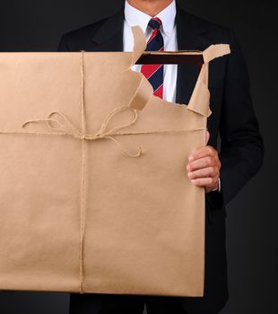 Closeup of a man holding a picture frame wrapped with brown paper in front of his body. Paper is torn revealing as see through hole with the man visible thru the opening..