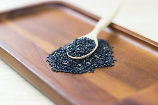 Black sesame seeds in wooden spoon pile on wood table 