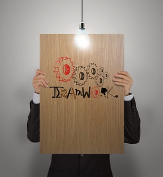 man showing poster of hand drawn word TEAMWORK with growing lightbulbon wooden board as concept 