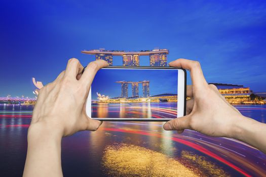 Girl taking pictures on mobile smart phone in Singapore cityscape night view
