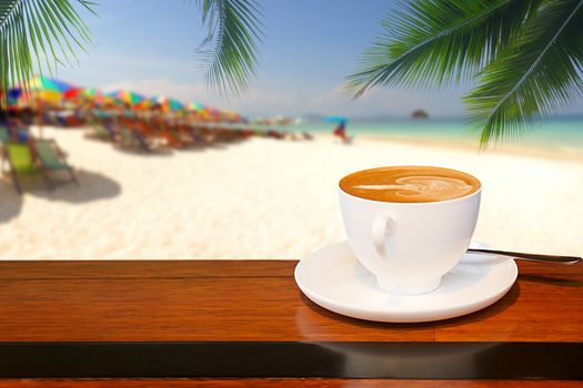 A cup of coffee resting on a wooden table with a coconut leaf background and blurred beach