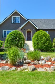 Nicely landscaped front yard of residential house with white steps leading to the main entrance. Front yard of family house with nice landscaping on blue sky background