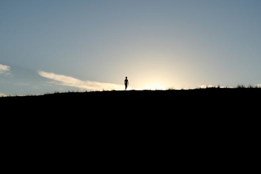Young boy silhouetted against the sun atop a dune in the desert