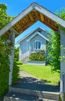 Look through the wooden gate on the pathway leading to small family house with nice lawn on the front yard