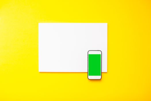 blank white sheet and smartphone on a bright yellow background. Mockup