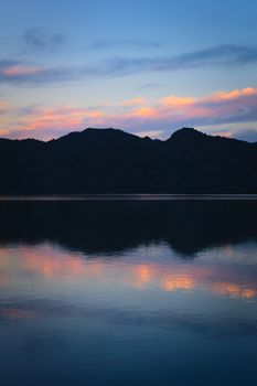 Blue twilight sky and dark mountains reflected on the calm waters of a lake. Calm, peaceful scene.