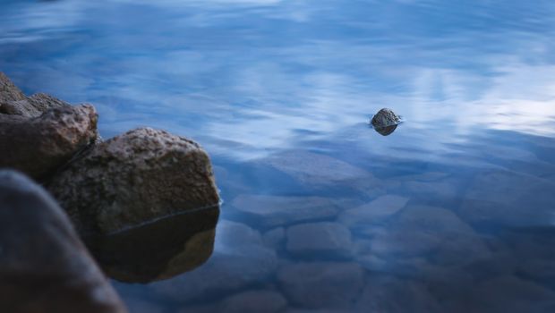 Natural stones on the shore of a lake at dusk. Tranquil scene, relaxing calm, zen meditation background.