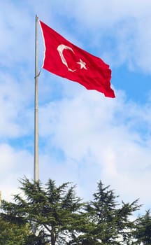 Turkish flag waving against blue cloudy sky.
