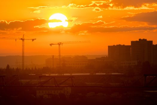 Bright orange sunrise shines on the industrial construction site. Mid shot