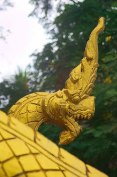 Gilded sculpture of a Naga serpent, a mythological protector creature, at the entrance of a Buddhist temple in Luang Prabang, Laos.