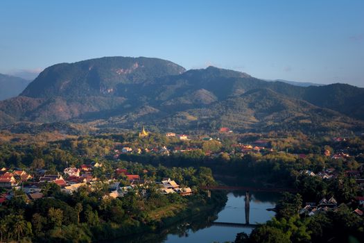 Elevated view of the city of Luang Prabang, Laos, traversed by the Nam Kham river and surrounded by thick rainforest, in the afternoon.