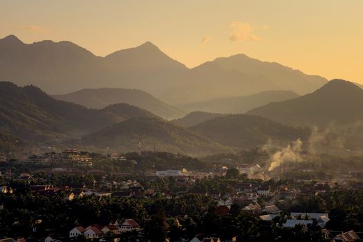 Elevated view of the city of Luang Prabang, Laos, at sunset, with mountains on the background.