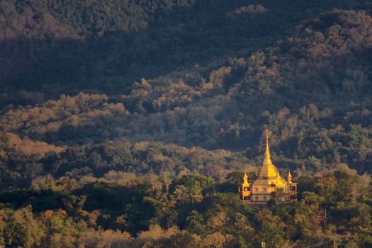 Golden buddhist temple standing out from the surrounding forest in the outskirts of Luang Prabang, Laos.