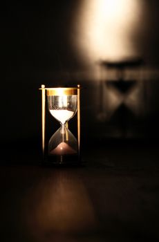 Vintage hourglass on wooden table against dark background with shadow