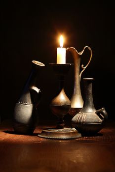 Set of nice ancient vases near lighting candle on dark background