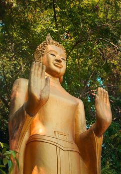 Golden statue of standing Buddha in the jungle, on the way to the top of Mount Phou Si, a sacred mountain in Luang Prabang, Laos.