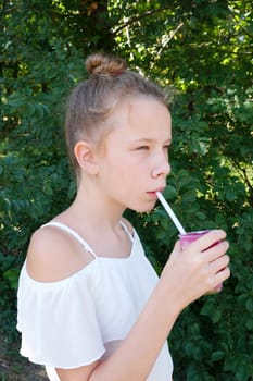 girl drinks fruit juice through a straw in summer park.