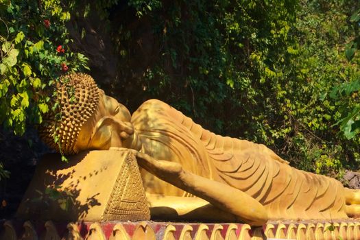 Golden statue of reclining Buddha on the way to the top of Mount Phou Si, a sacred mountain in Luang Prabang, Laos.