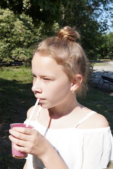 girl drinks fruit cocktail through a straw in a park on a sunny day.