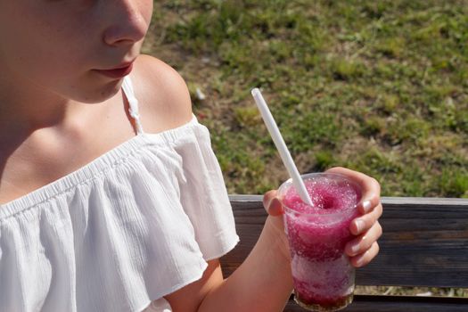 refreshing fruit drink with a straw in the hands of a girl in the park.