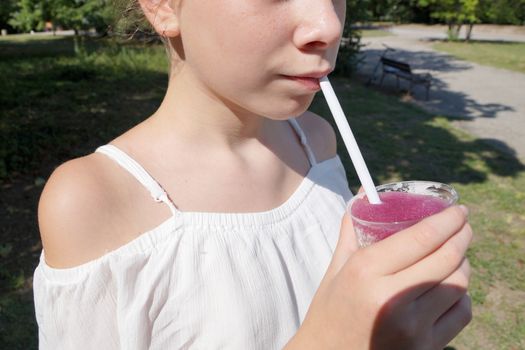 girl drinks fruit cocktail through a straw in a park on a sunny day.