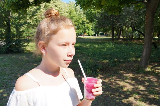 girl holding fruit cocktail with a straw in the park on a sunny day.