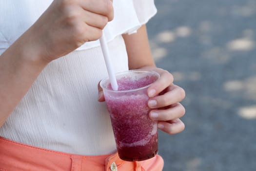 girl holding fruit cocktail with a straw in the park on a sunny day.