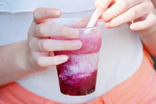 refreshing fruit drink with a straw in the hands of a girl in the park.