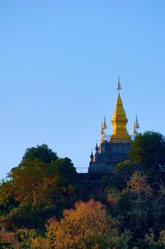 Golden buddhist stupa of Wat Chom Si at the summit of Mt. Phou Si, in Luang Prabang, Laos. Low angle view from the city.