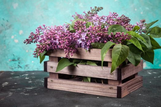 Purple lilac flowers bouquet on wooden box on black concrete background. Stylish floral greeting card. Happy mothers day.