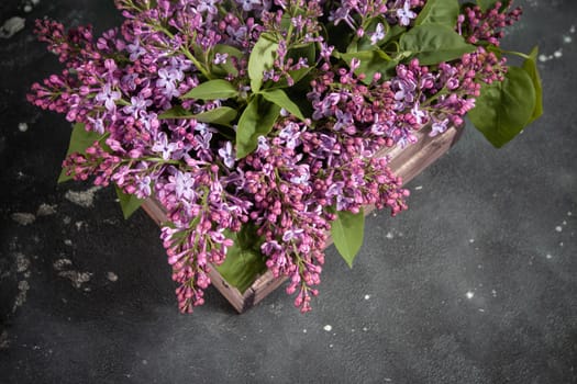 Purple lilac flowers bouquet on wooden box on black concrete background. Stylish floral greeting card. Happy mothers day.