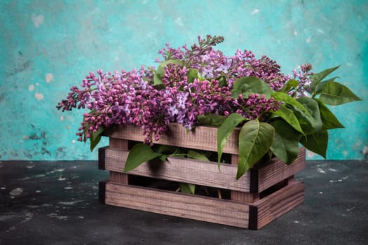 Purple lilac flowers bouquet on wooden box on black concrete background. Stylish floral greeting card. Happy mothers day.