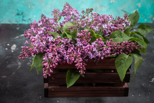 Purple lilac flowers bouquet on wooden box on black concrete background. Stylish floral greeting card. Happy mothers day.