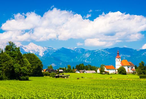 Beautiful Alpine village in Slovenia. Mountains and cloudy sky. Green meadow and the old Church