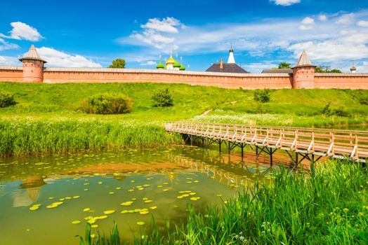 Suzdal cityscape on a summer day. Panorama of the old Russian historic town with traditional architecture and wooden bridge across the river. The Golden Ring of Russia.