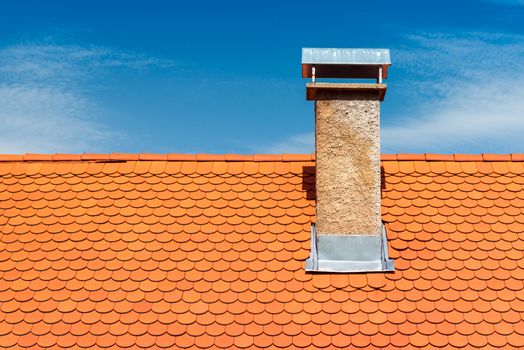 Modern roof with chimney. Orange ceramic tile, shingle. Blue sky on the background
