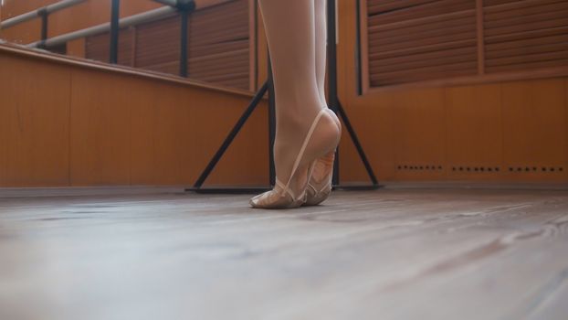 Ballet dancer's feet in scenic shoes training in studio, close up view
