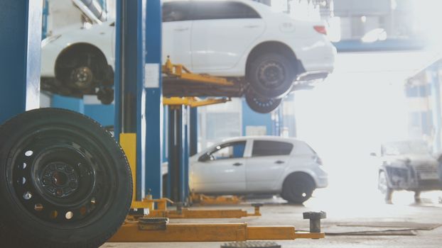 Car in auto service lifting for repairing, mechanics in garage, close up