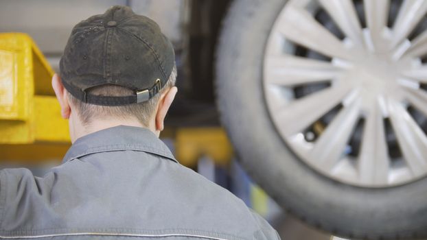 Rear view of mechanic near car on the lift in a service station, close up